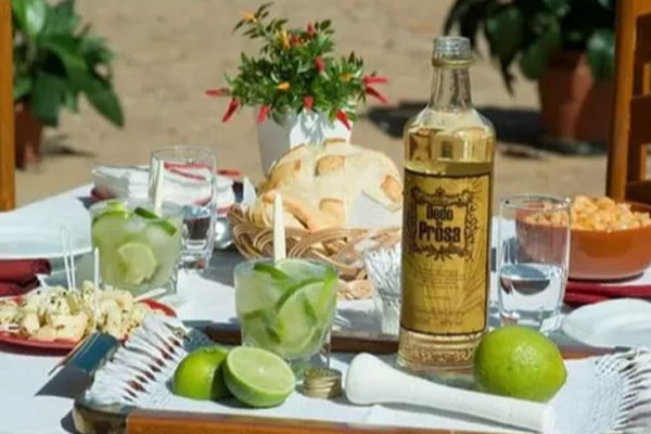 Mesa com uma garrafa da cachaça mineira Dedo de Prosa e alguns limões para preparar uma caipirinha