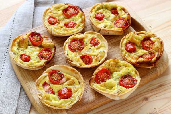 Tortinhas de queijo com tomate seco sobre uma tábua de madeira marrom para servir na festa infantil fazendinha