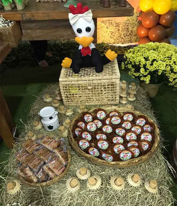 Rolinhos de melzinho e paçocas de rolha dentro do chapéu de palha e da peneira fazendo parte da decoração de uma festa infantil de fazendinha