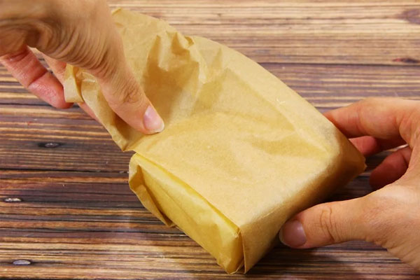 Mão feminina enrolando um pedaço de queijo parmesão em papel parafinado e mostrando como conservar queijo parmesão corretamente