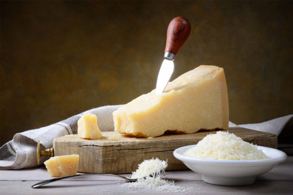 Tábua com um pedaço de queijo parmesão e um prato branco do lado cheio de parmesão ralado na hora