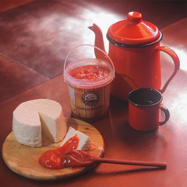 Mesa de café da tarde em Minas Gerais, com um bule e uma xícara de café, um pedaço de queijo mineiro e uma goiabada cascão de colher