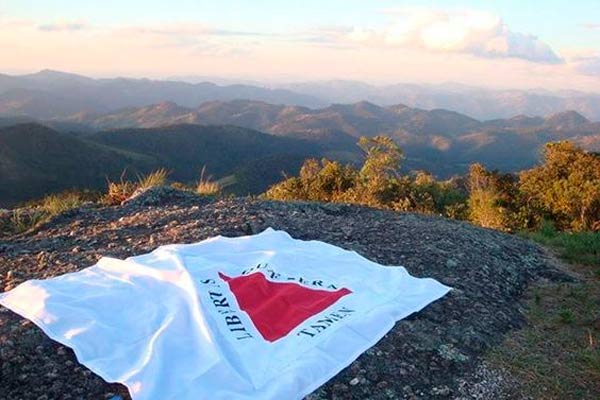 Bandeira de Minas Gerais estendida no topo da montanha e ao fundo a paisagem das montanhas de Minas